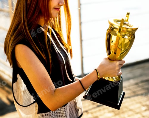 Preview: Asian teenage girl in sporty clothes holding a trophy outdoors