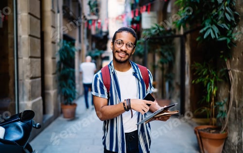 Preview: Cheerful ethnic hipster with smartphone and tablet on street
