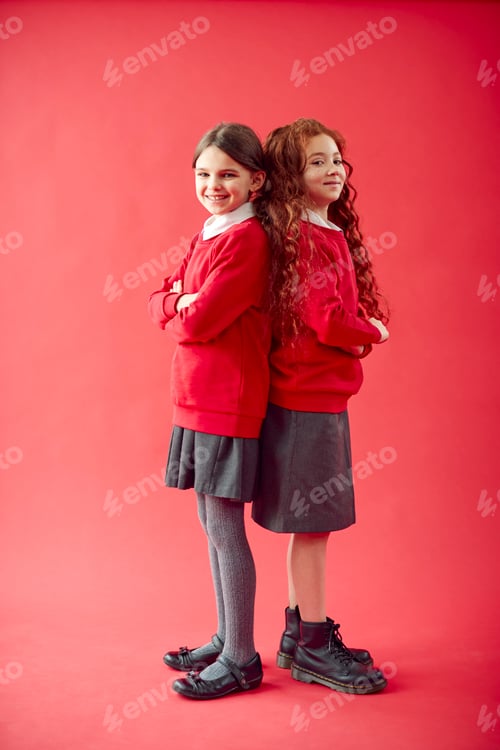 Preview: Two Elementary School Pupils Wearing Uniform Back To Back Against Red Studio Background