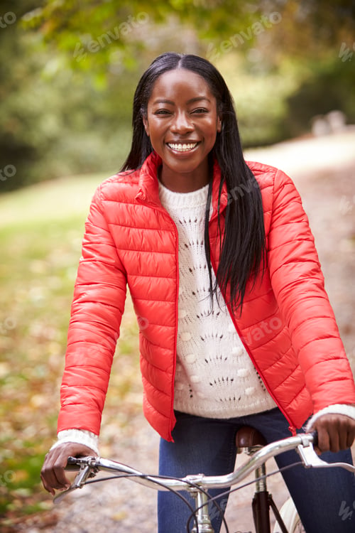 Preview: Young adult black woman sitting on a vintage bicycle in a park smiling to camera
