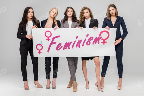 Preview: attractive businesswomen holding large sign with feminism lettering on grey background