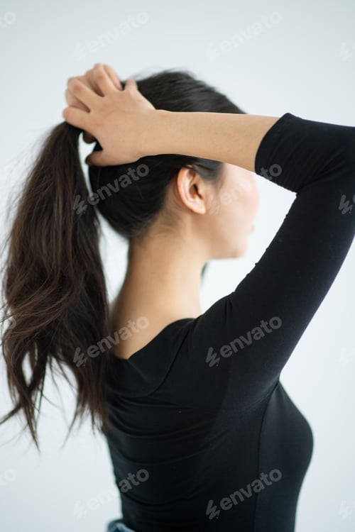 Preview: Woman styling her hair in ponytail indoors