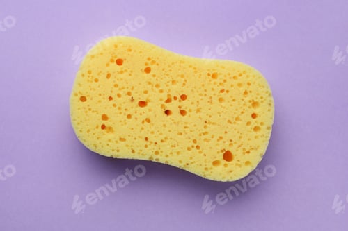 Preview: New yellow sponge on violet background, top view