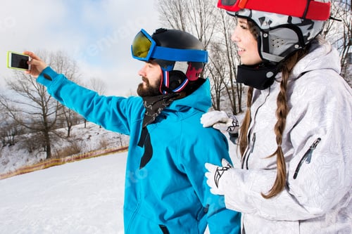 Preview: Young smiling couple of snowboarders taking selfie with smartphone