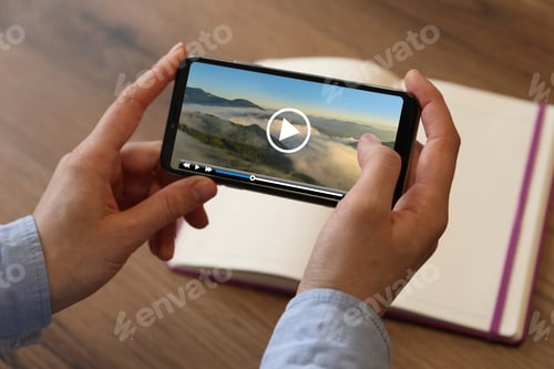 Preview: Woman watching video on mobile phone at wooden table, closeup