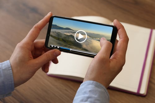Woman watching video on mobile phone at wooden table, closeup