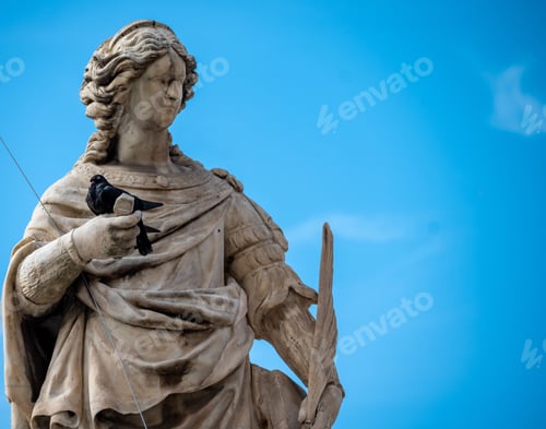 Preview: Vintage-style statue of a man with a small bird perched on it on the backdrop of a clear blue sky