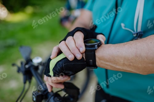 Preview: Close-up of senior man biker setting and looking at sports smartwatch, checking his performance.