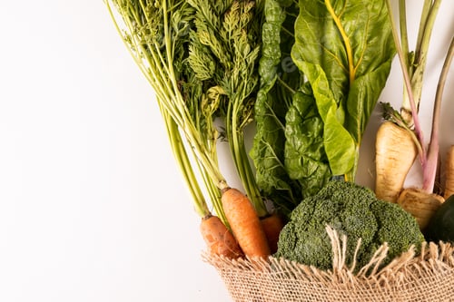 Preview: Overhead view of fresh organic vegetables with burlap on white background, copy space