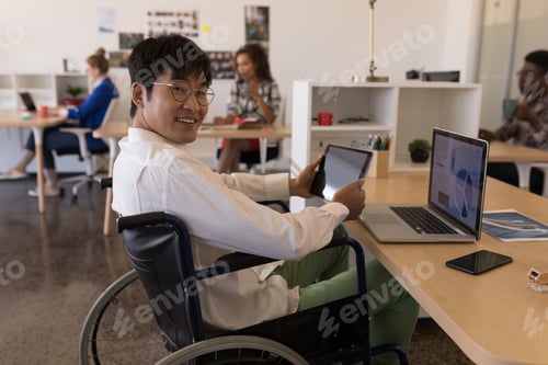 Preview: Side view of young disabled Asian male executive using digital tablet at desk in modern office