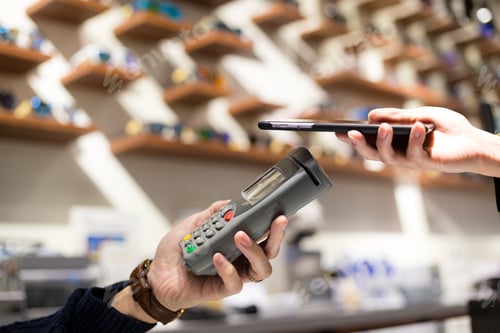 Preview: Woman pay by NFC on mobile phone in spectacle shop