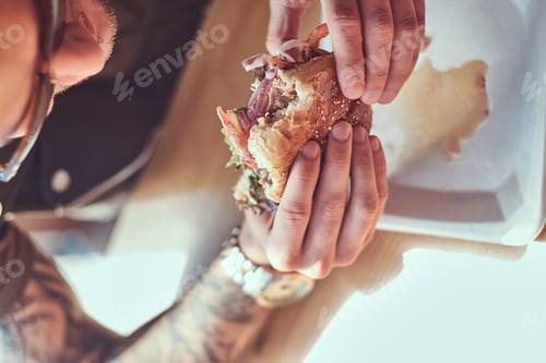 Preview: Handsome hipster sits at a table, decided to dine at a roadside cafe, eating a hamburger.