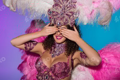 Preview: Cheerful woman in carnival costume with pink feathers covering her eyes isolated on blue background