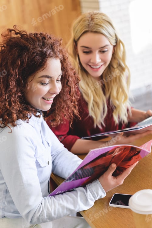 Preview: selective focus of attractive and smiling women reading magazines and talking at cafe