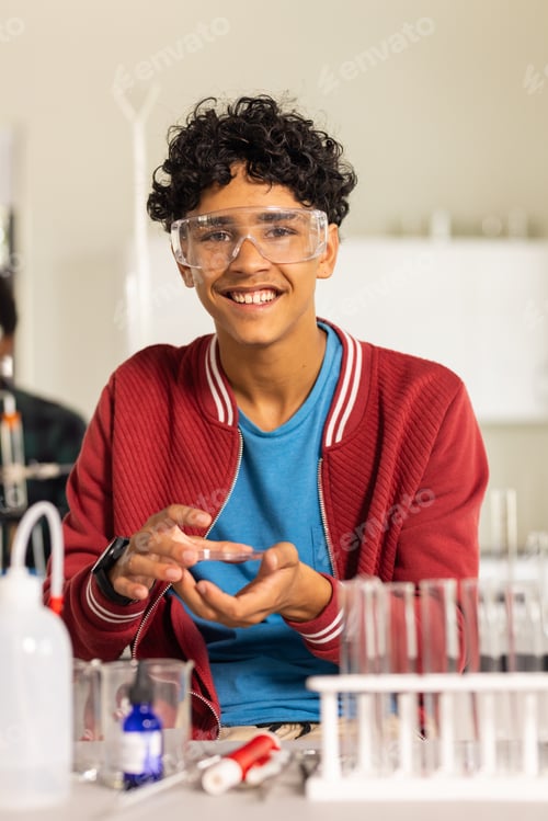 Preview: Wearing safety goggles, teenager conducting science experiment in high school classroom