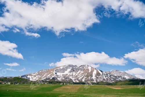 Preview: Green pasture at the foot of a mountain range covered with snow