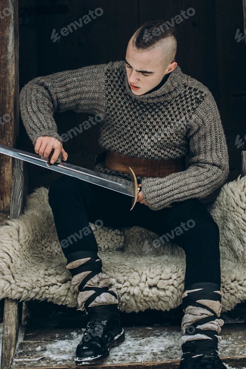 Preview: Portrait of strong viking warrior sharpening his sword, scandinavian viking cosplay