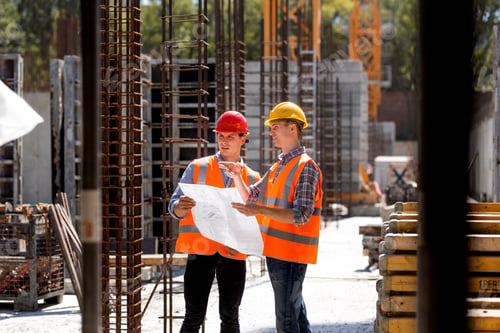 Preview: Construction manager and engineer dressed in orange work vests and hard helmets explore construction