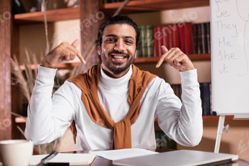 Preview: Indian teacher pointing at himself and laptop recommending e-learning indoors