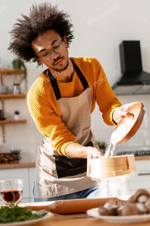 Preview: Young man sifting flour, preparing dough for traditional baking in home kitchen