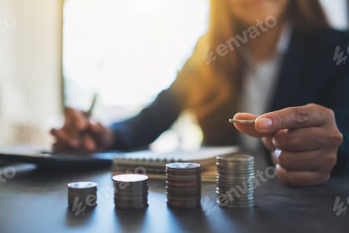 Preview: Businesswoman holding and stacking coins while calculating money on the table