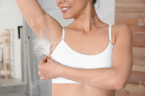 Preview: Woman touching armpit with feather at home, closeup. Epilation procedure