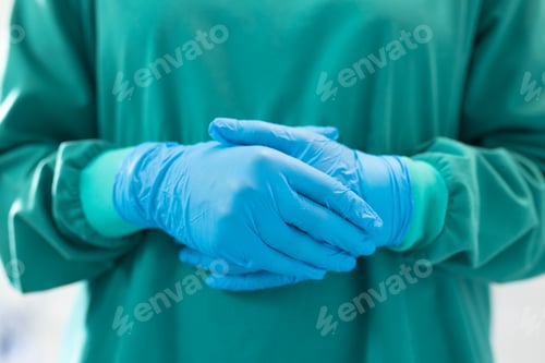 Preview: Midsection of female surgeon ready for operation in blue surgical gloves and green gown