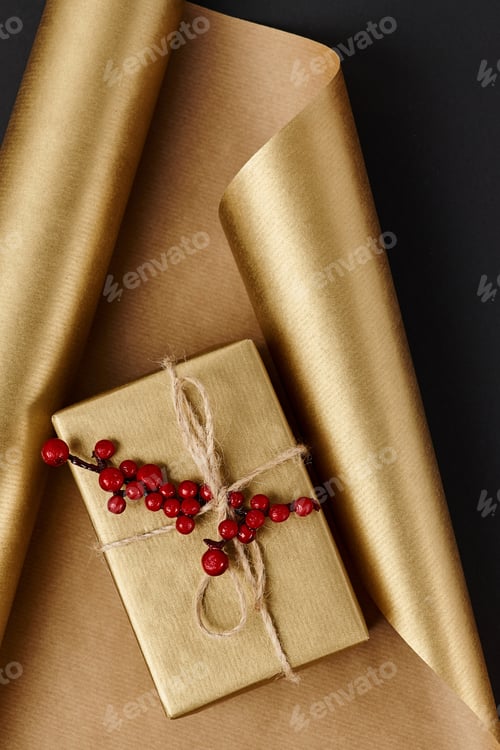 Preview: golden gift box with red holly berries on shiny wrapping paper and black backdrop, Christmas decor