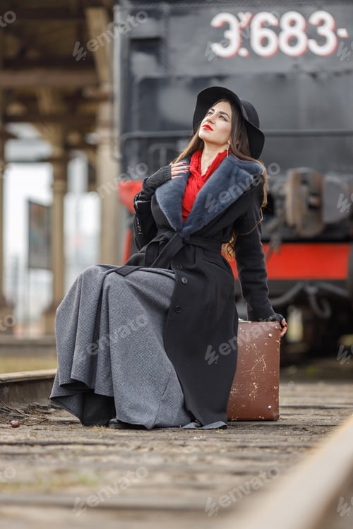 Preview: A girl in a black coat and hat with a suitcase near an old steam locomotive.Vintage portrait