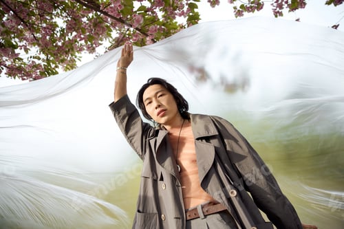 Preview: Stylish young man enjoys a serene moment in a park under cherry blossom trees