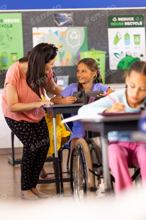 Preview: Diverse female teacher and schoolgirl using tablet in elementary school class