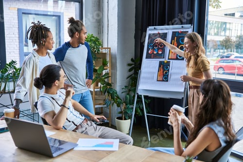 Preview: businesswoman pointing at flip chart and discussing startup project with multiethnic colleagues