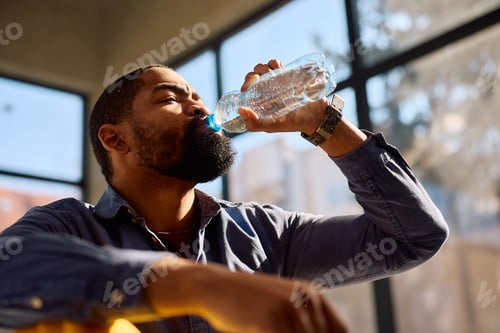 Preview: Thirsty black construction worker having water break at work.