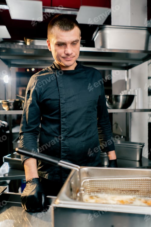Preview: chef in the kitchen in black jacket smiling looking at the deep fryer and sweet potato close-up