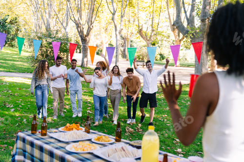 Preview: Friends walking towards table at a park party, celebrating and raising arms