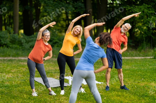 Preview: Group of seniors following yoga stretch routine outdoors, led by younger instructor