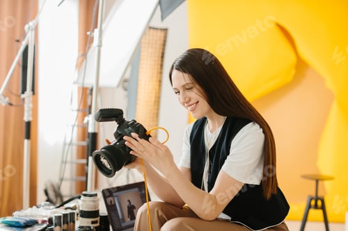 Preview: Female photographer with a camera sits on her desk and looks at the pictures after a photo shoot.