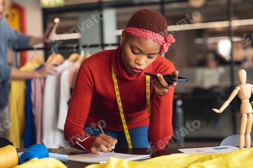 Preview: African american young female fashion designer taking order through mobile phone in studio office