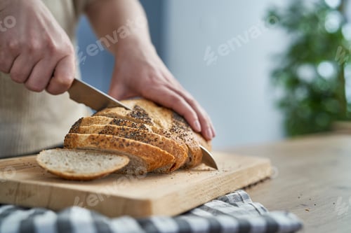 Preview: Close up of woman cutting bread in slices on wooden board