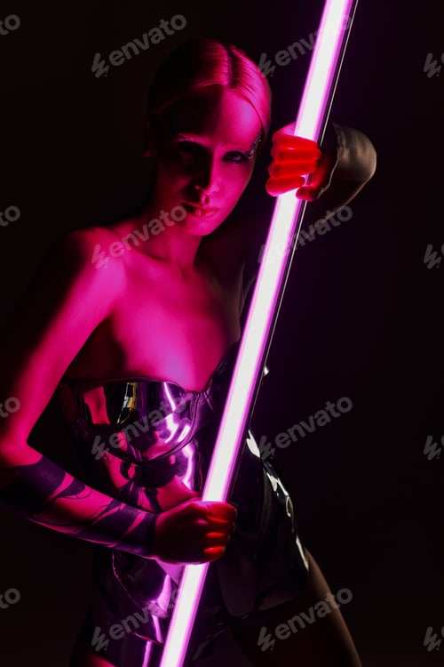 Preview: peculiar woman in metallic futuristic attire holding pink LED lamp stick and looking at camera