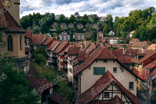 Preview: Scenic view of Bern\'s charming rooftops and hillside homes under a cloudy sky