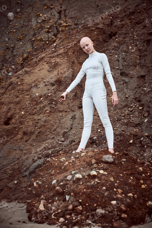 Preview: Full length portrait of young hairless girl with alopecia in white suit holding handful of earth