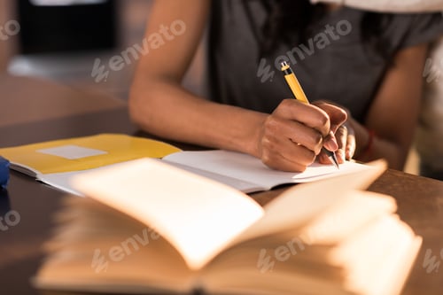 Preview: partial view of woman sitting at table and writing in notebook at home
