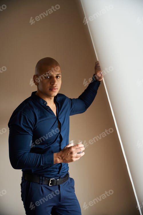 Preview: African american businessman with glass of water looking at camera by window