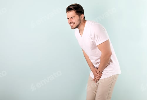 Preview: Young man with urological problems suffering from pain on color background