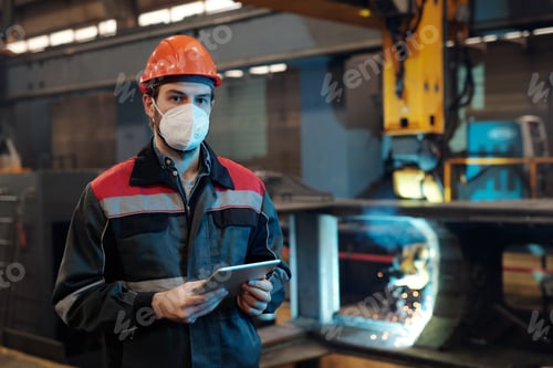 Contemporary factory engineer in protective workwear holding digital tablet