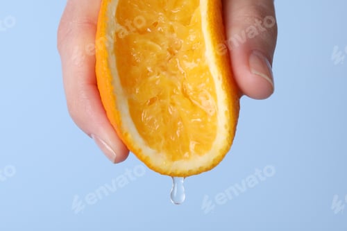 Preview: Woman squeezing juicy orange on light blue background, closeup