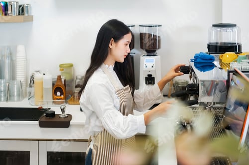 Preview: Young cheerful barista wearing apron while preparing coffee at an automatic machine.