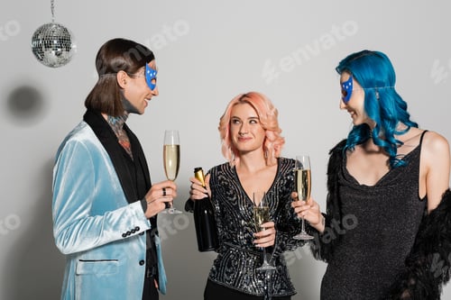 Preview: queer person holding champagne bottle near nonbinary friends in party masks on grey background