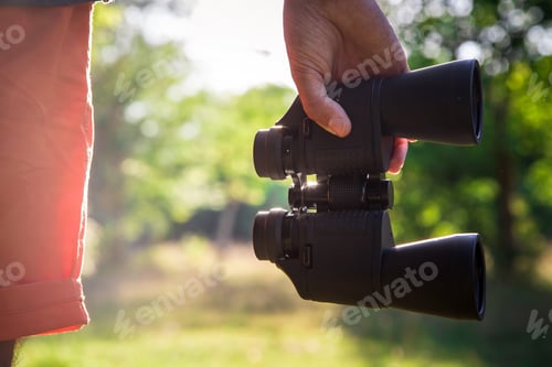 Preview: Male hiker looking through binoculars in forest